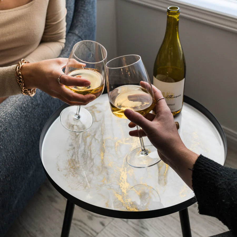 Two people toasting with wine glasses on a small round resin table.