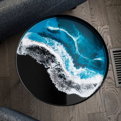 Round small resin table with a blue and white wave design on a wooden floor.