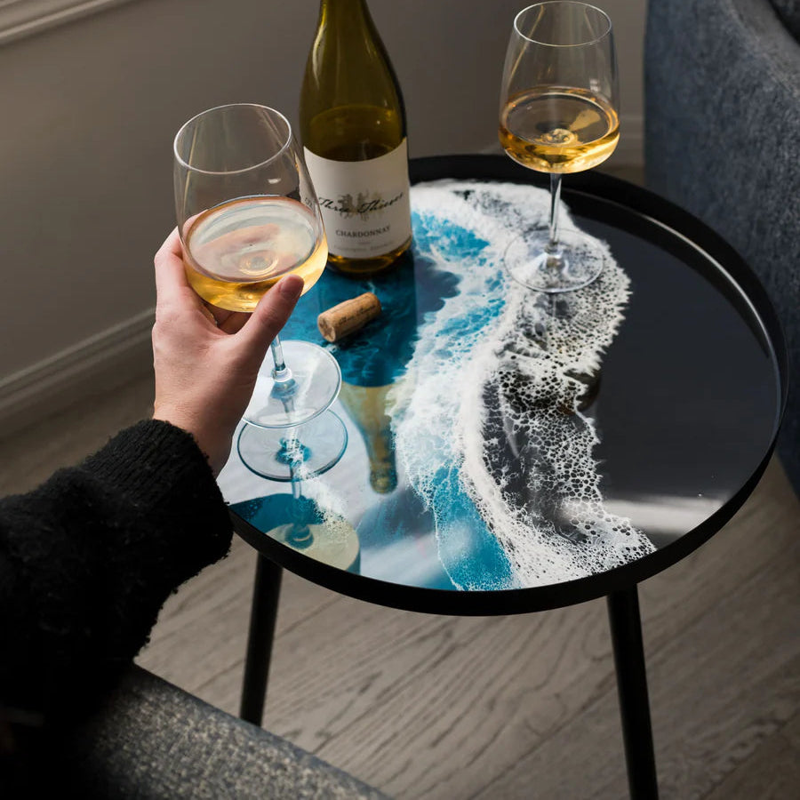 Person holding a glass of white wine next to a bottle on a decorative small resin table.