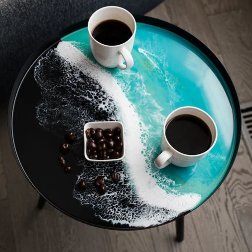 Round resin table with coffee-themed decor including two cups of coffee and a small container of coffee beans.