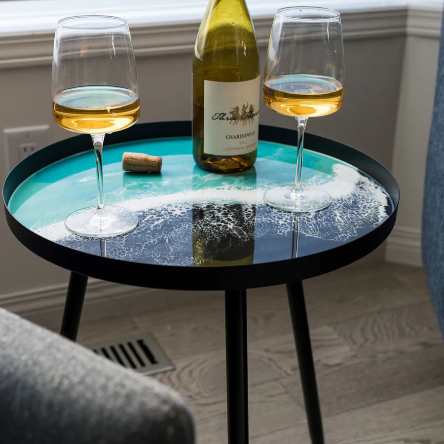 Small round resin table with two wine glasses and a bottle on a wooden floor.