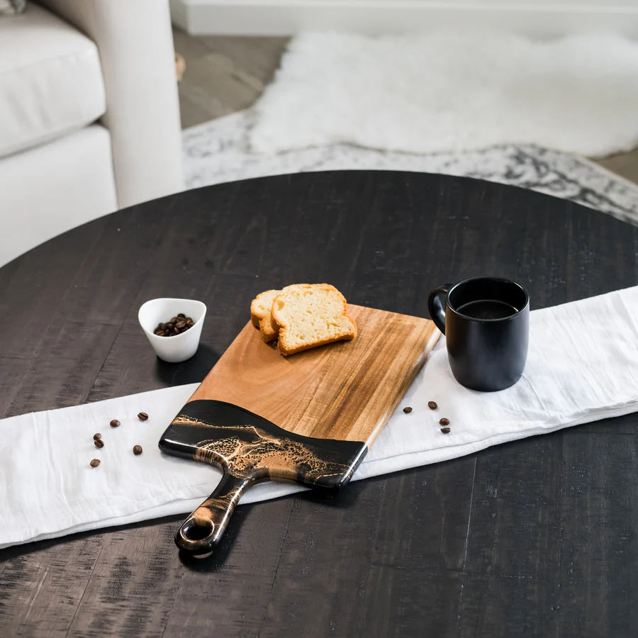 Wooden resin charcuterie board with toast and a black mug on a dark wooden table.