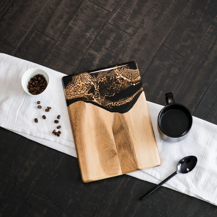 Wooden resin charcuterie board with black resin design on a dark surface with coffee beans and a mug.