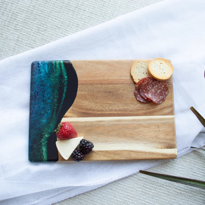 Wooden resin charcuterie board with a colorful resin design, placed on a white surface with a plant in the background.
