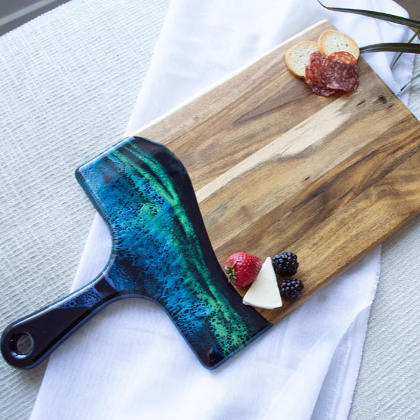 Wooden resin charcuterie board with a decorative handle on a light surface with fruits and bread.