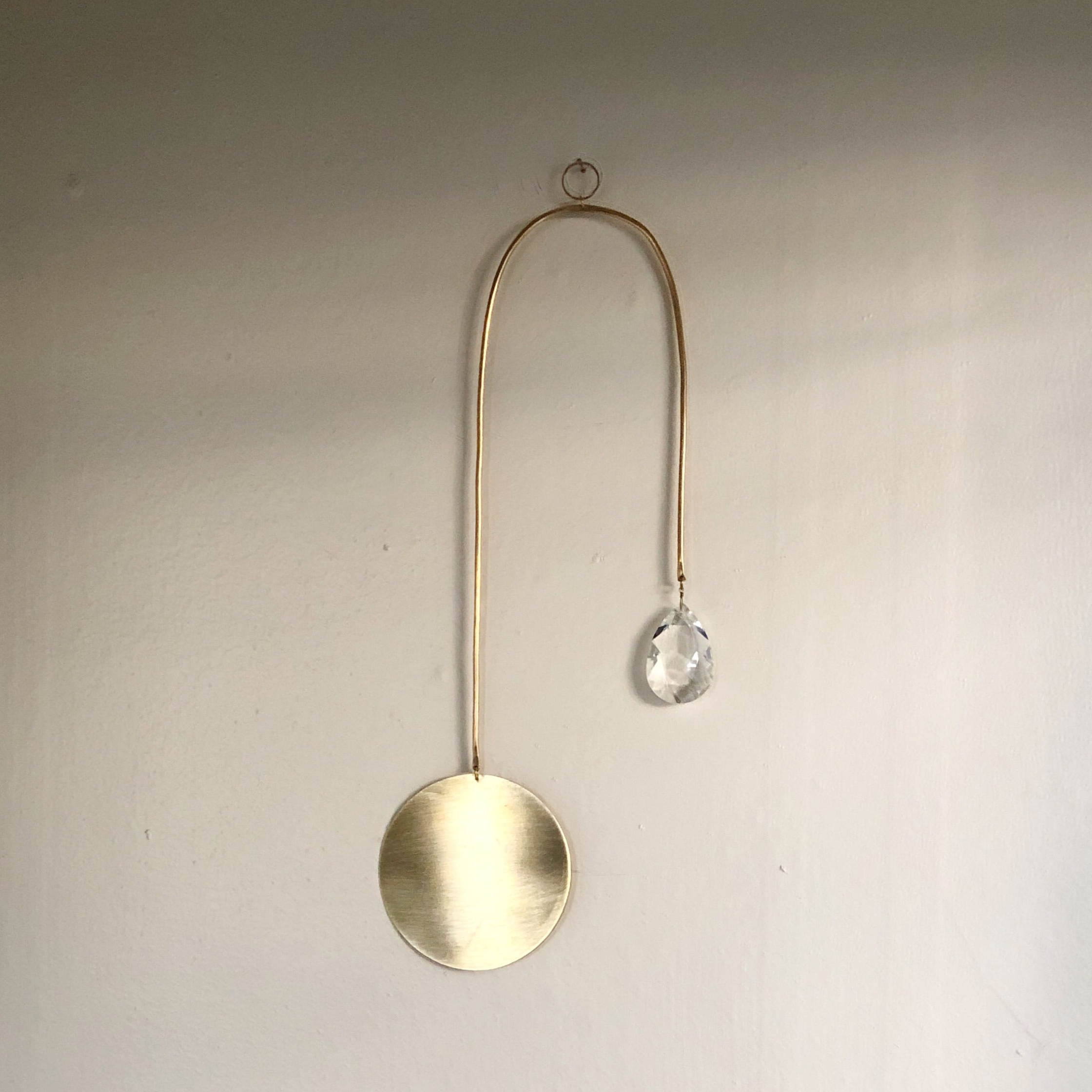 Golden Hour Suncatcher featuring hand forged brass wire and vintage glass crystal, displayed on wall