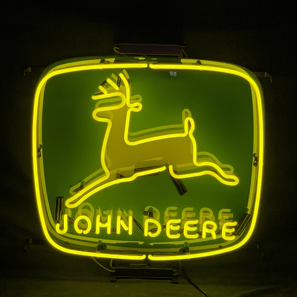 John Deere Neon Signs Light displaying a green and yellow neon tractor design on a metal grid backing, glowing brightly in an indoor setting.