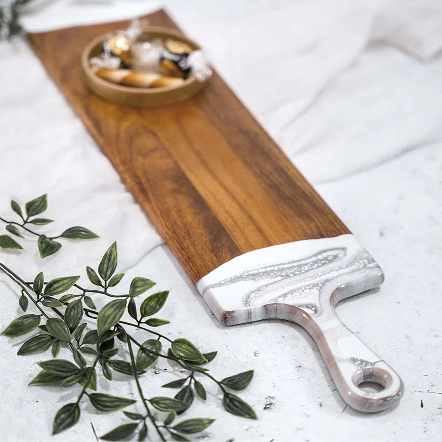 Wooden baguette resin serving tray with a decorative handle on a light surface with green leaves.
