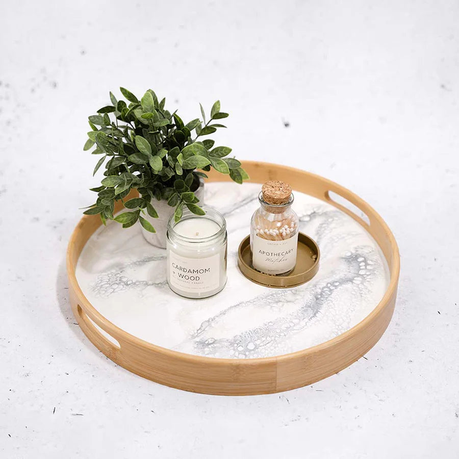 Round wooden resin serving tray with a candle, plant, and small bottle on a light background