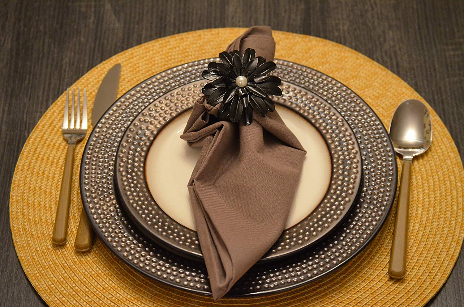 Set of four black floral napkin rings with pearl centers arranged on a neutral fabric