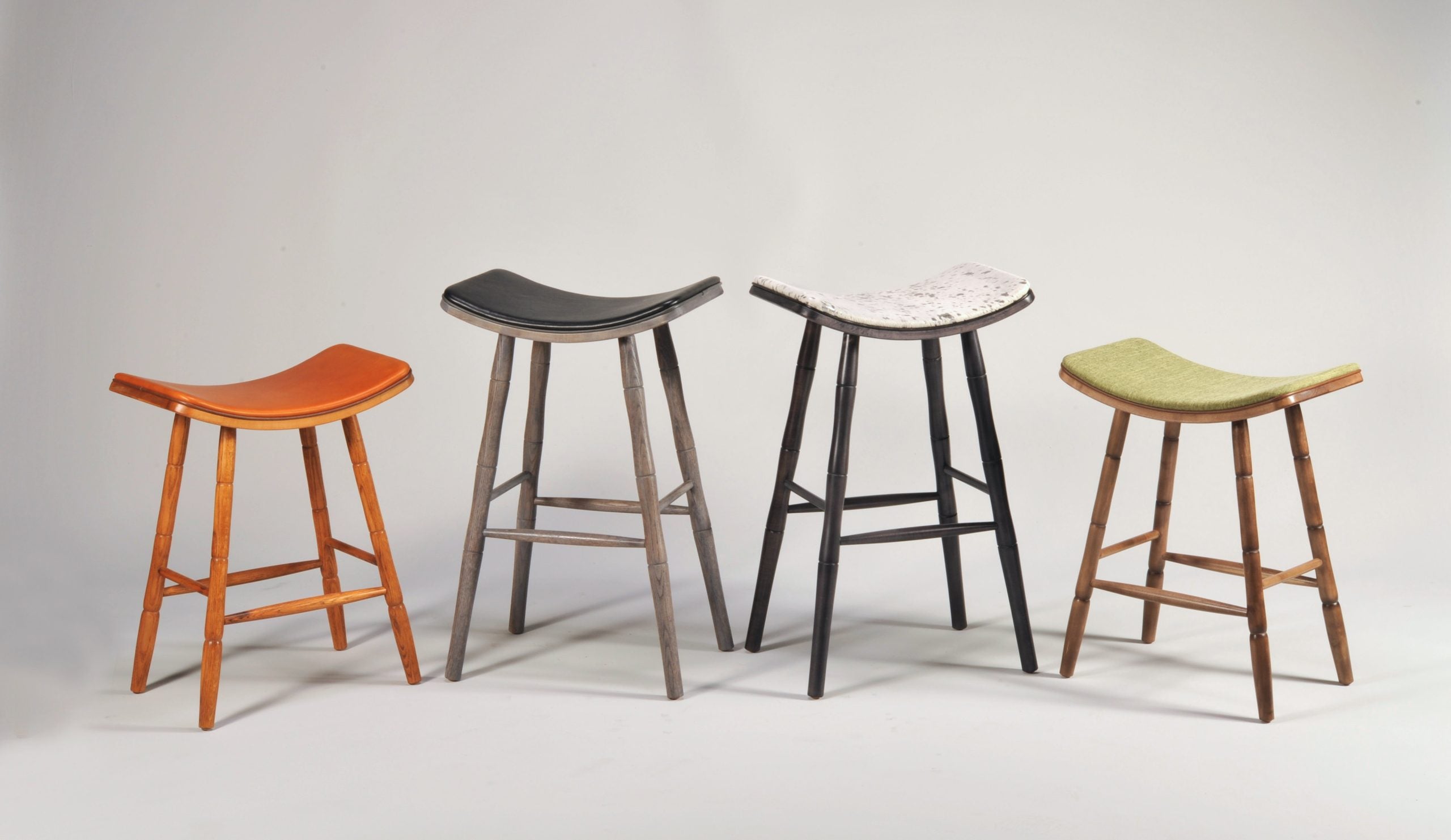EB Saddle Stools with turned wood legs and saddle-shaped seats upholstered in various materials