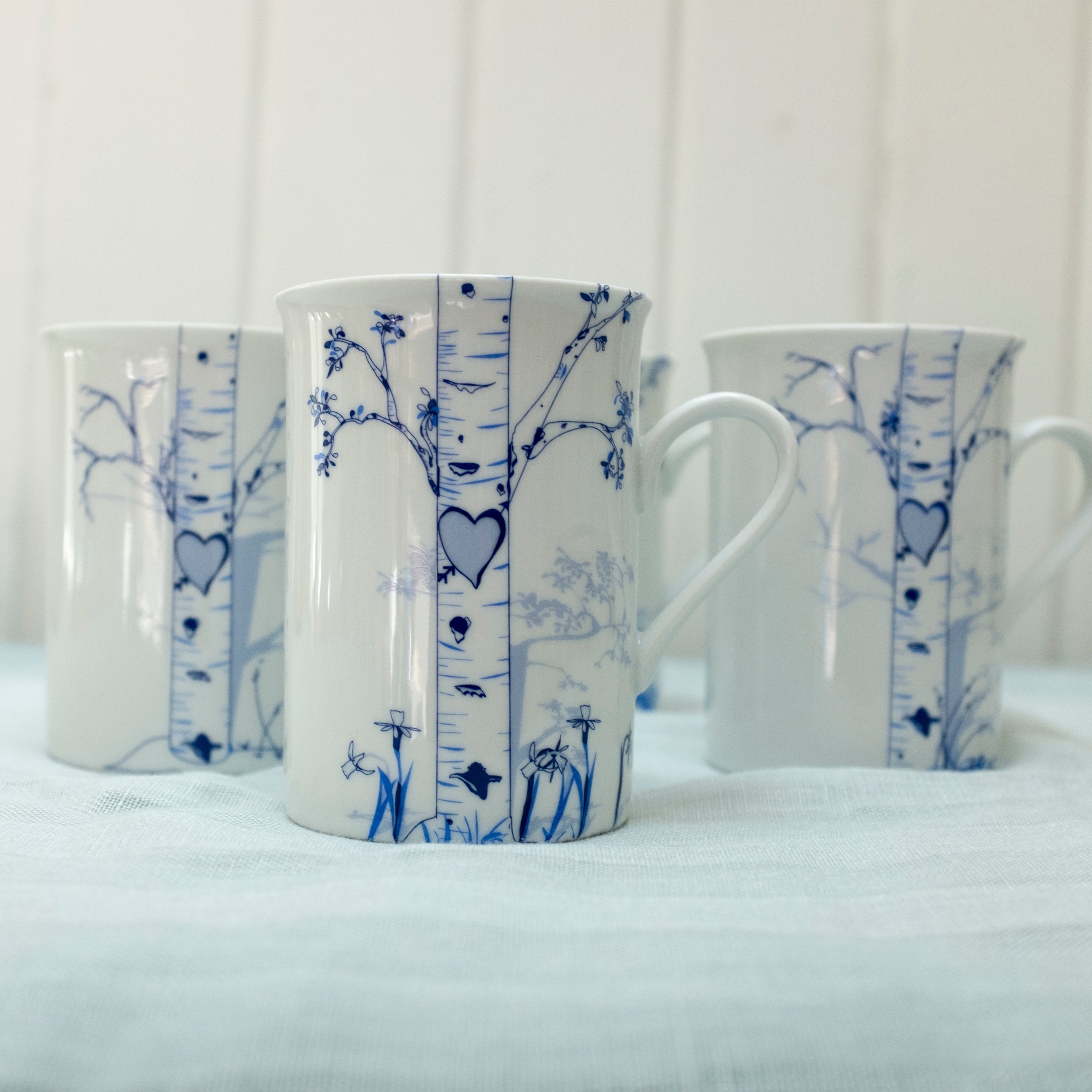 Set of ceramic mugs featuring hand-drawn birch tree seasonal designs with carved heart for initials