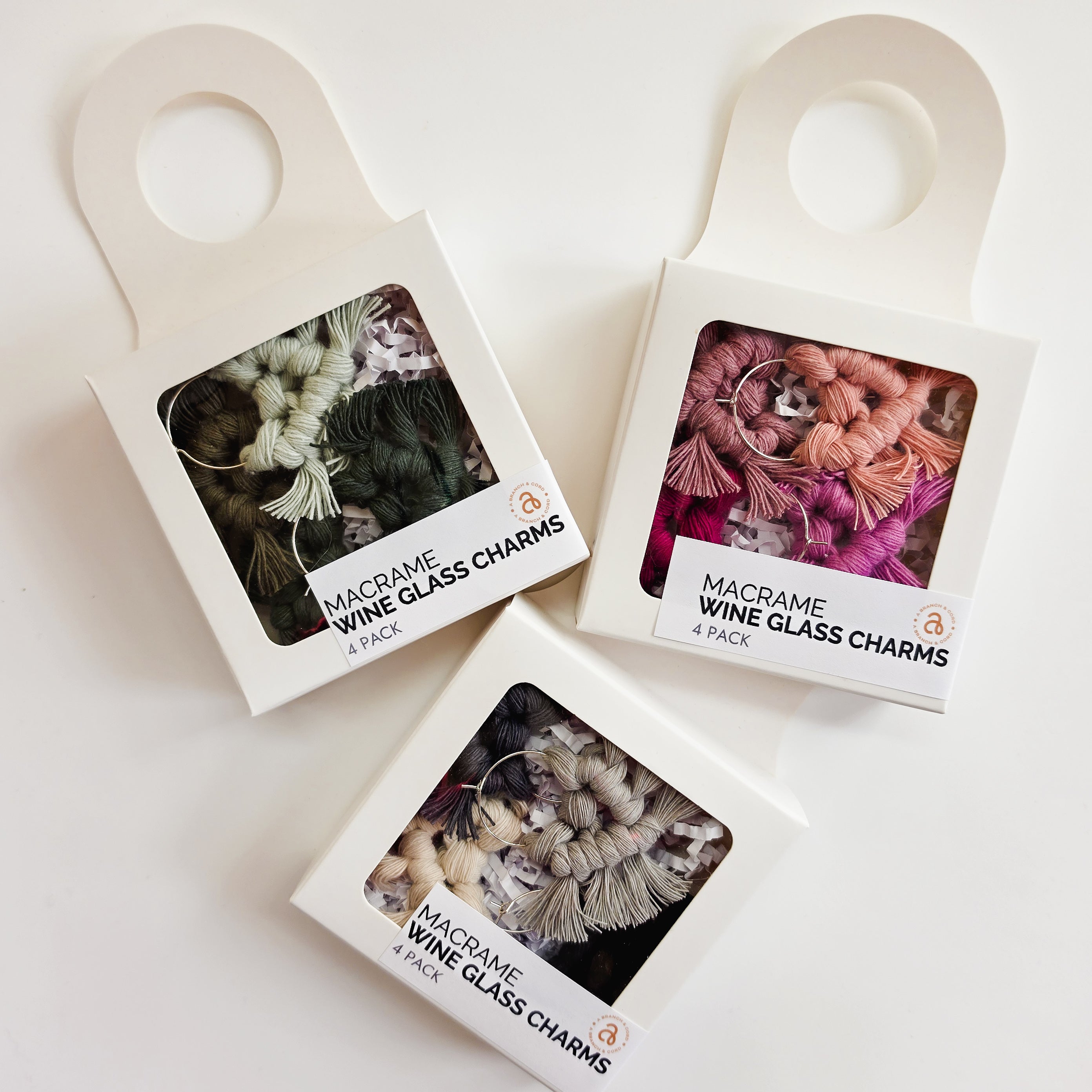 Set of four colorful macrame wine charms arranged on a textured wool surface