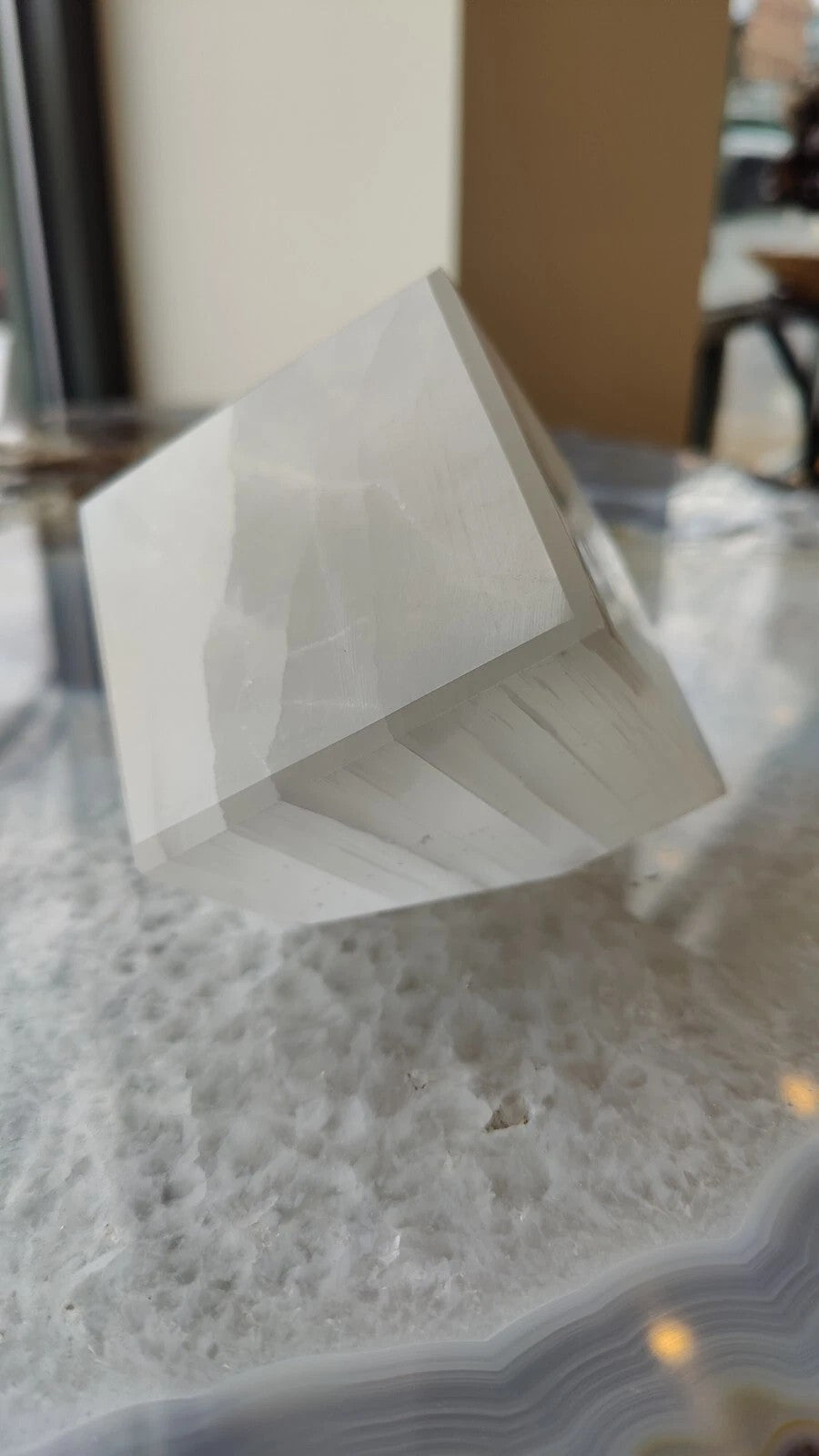 Polished translucent selenite cube standing on a wooden surface