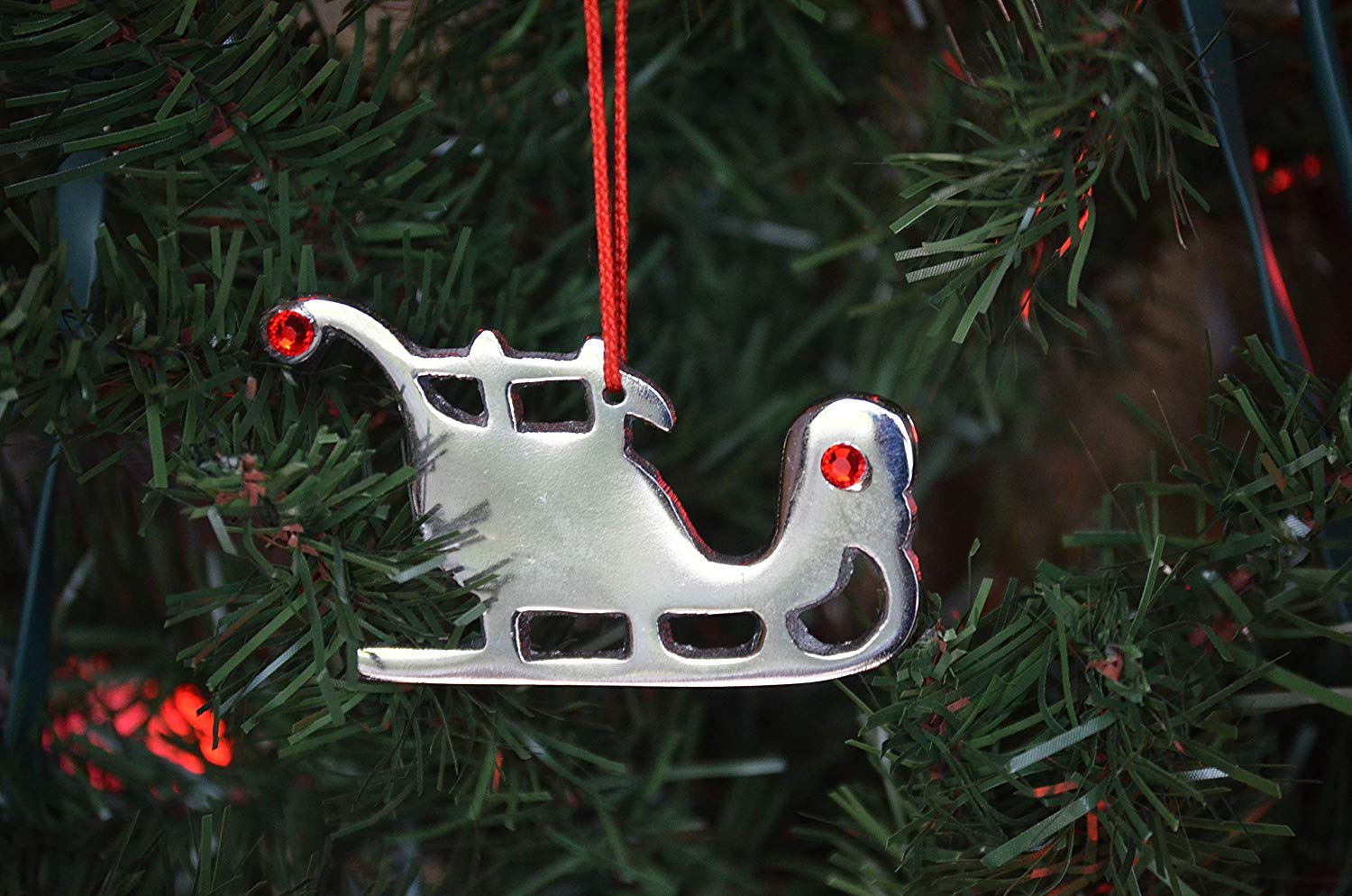 Set of four silver nickel finish sleigh Christmas tree ornaments each with red ruby crystals and red ribbons hanging on a holiday display.