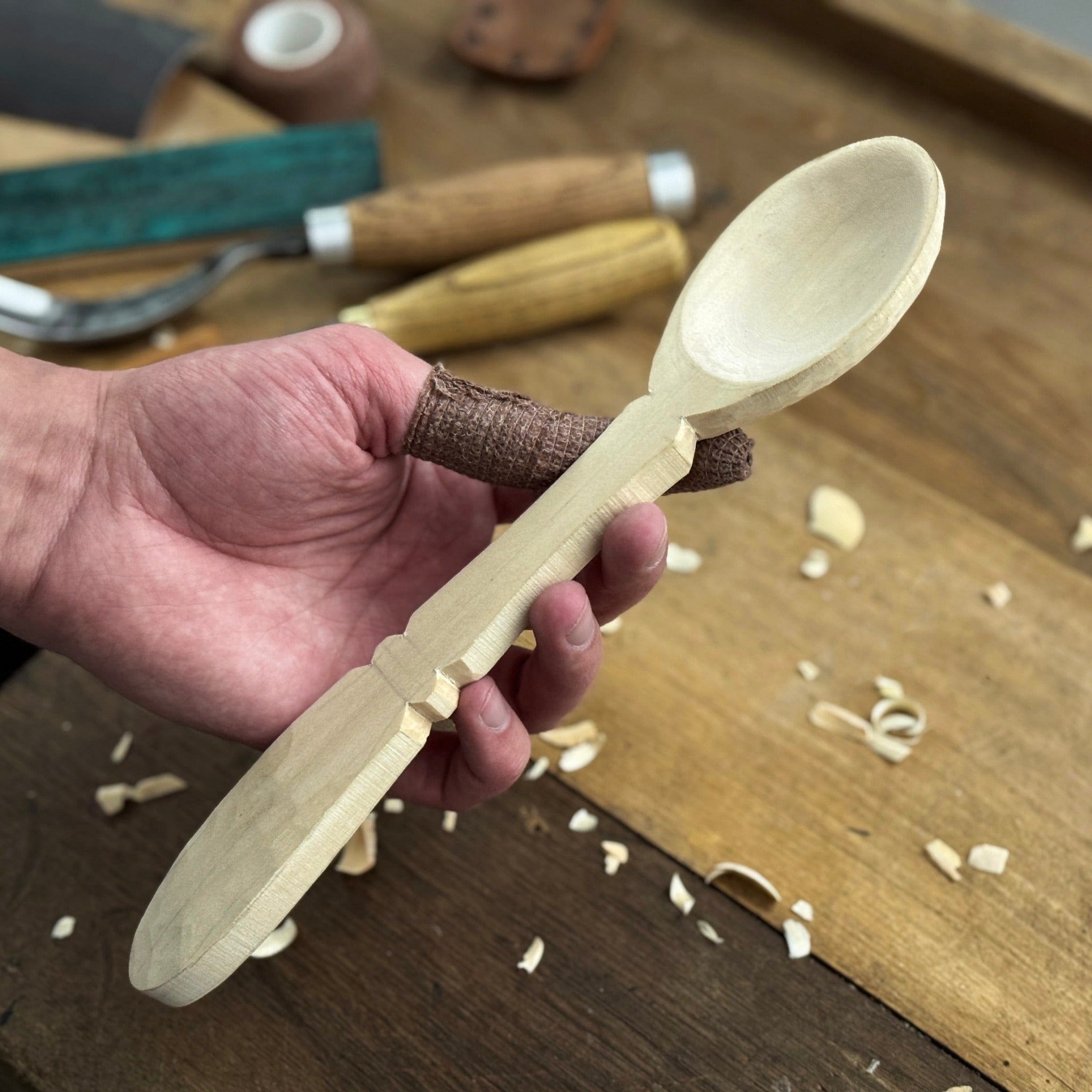 Complete Spoon Carving Kit with bent gouge, whittling knife, wooden blank, sandpaper, sharpening board, pencil, and finger wrap