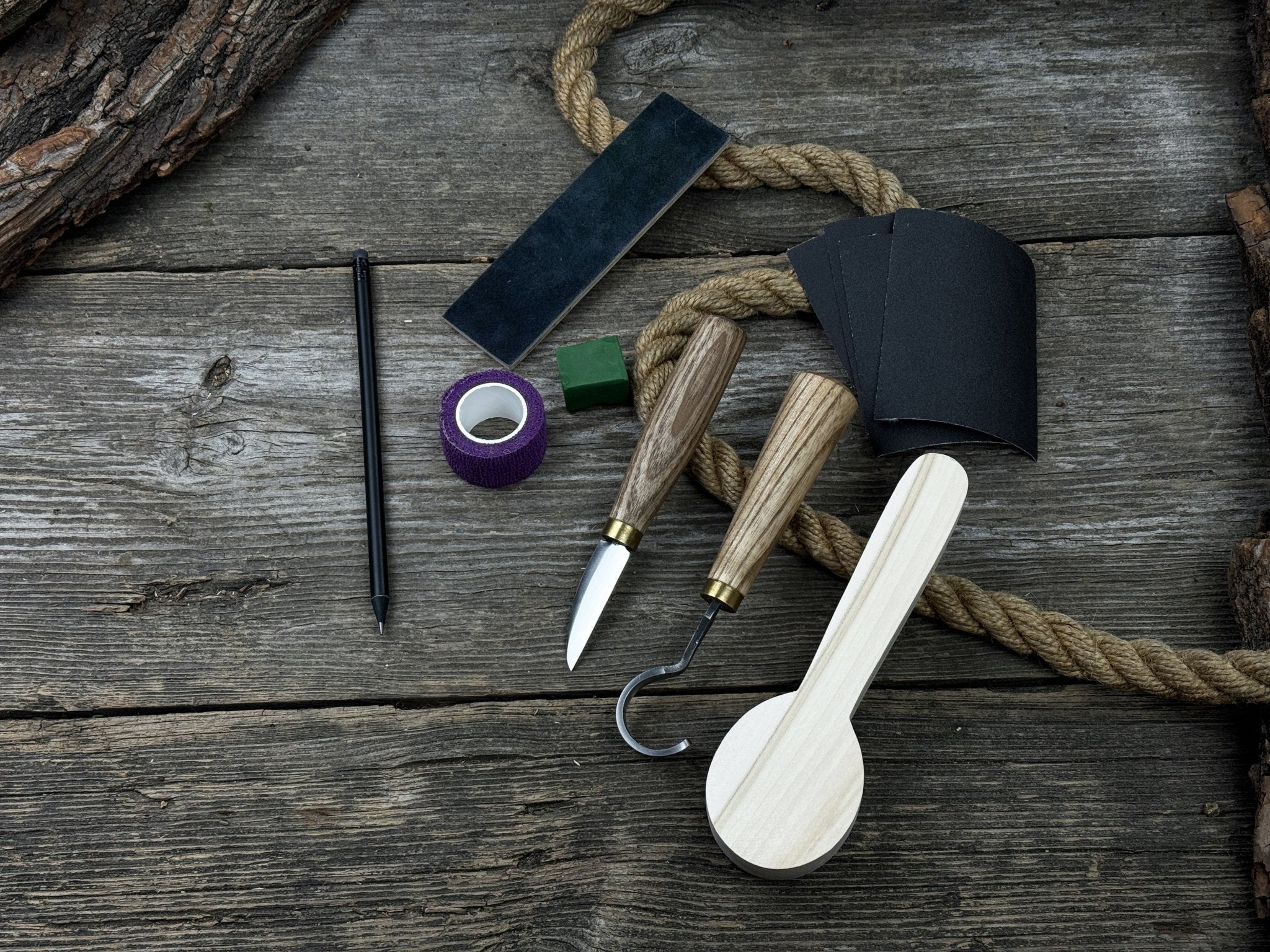 Spoon Carving Kit with knives, wooden blank, sandpaper, sharpening board, pencil, and finger wrap