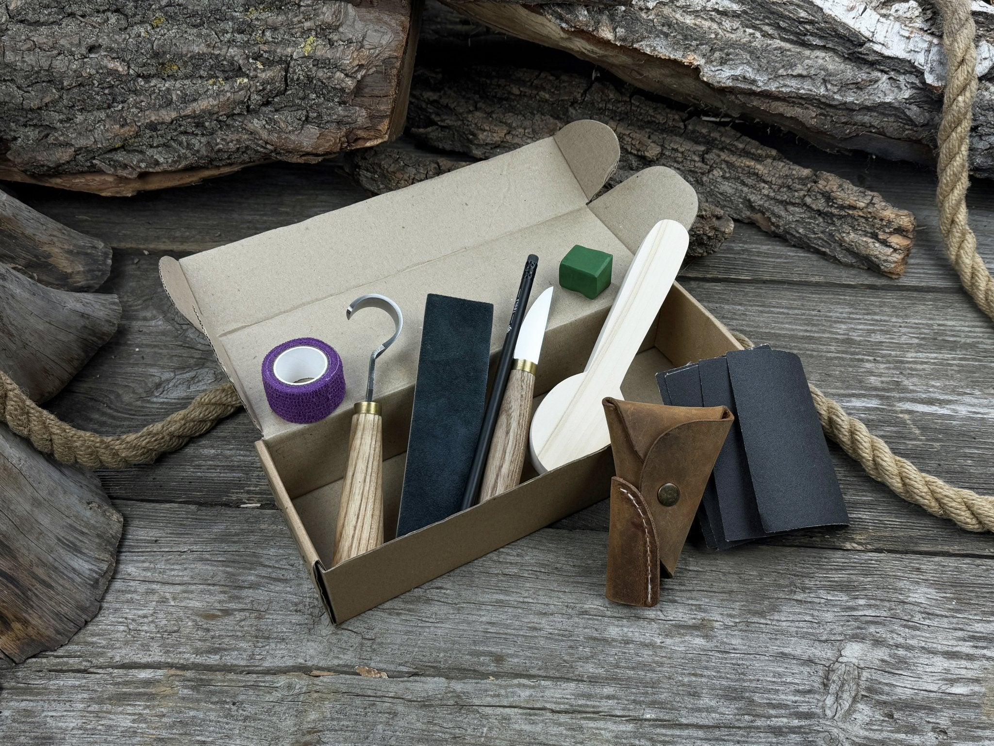 Spoon Carving Kit with knives, wooden blank, sandpaper, sharpening board, pencil, and finger wrap