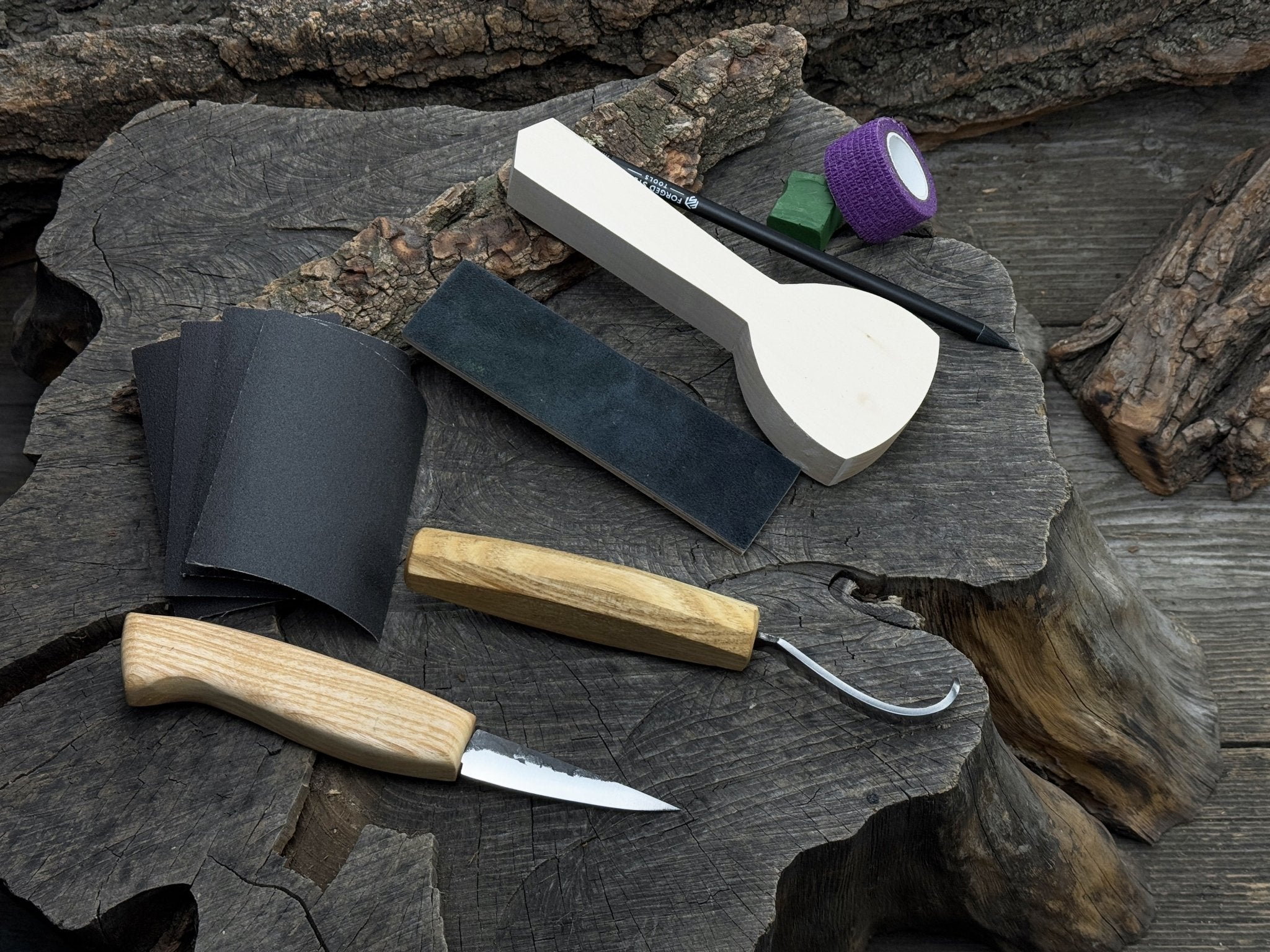 Beginner wood carving kit with sloyd knife, hook knife, wooden blank, sandpaper, sharpening board, pencil, and finger wrap