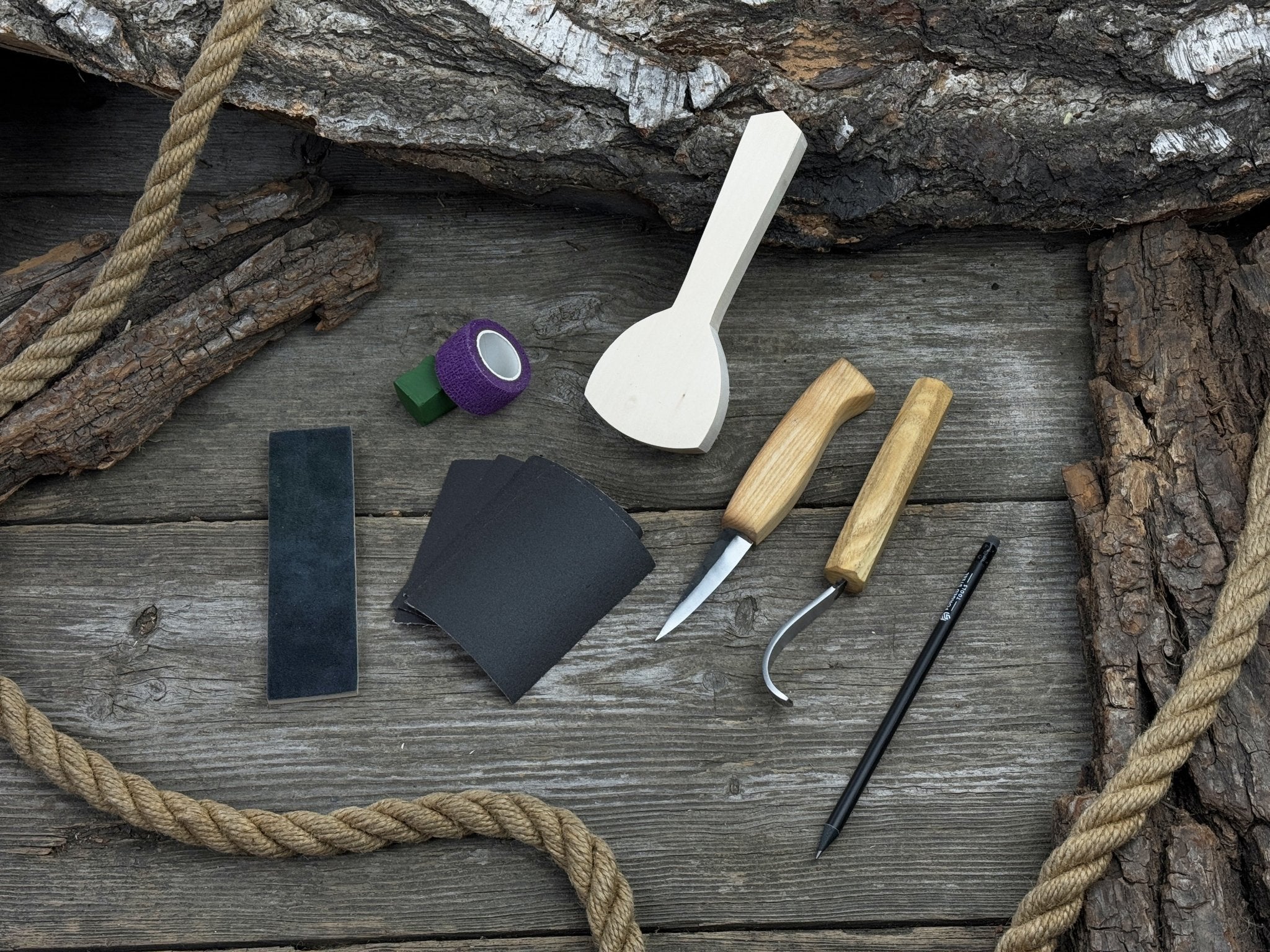 Beginner wood carving kit with sloyd knife, hook knife, wooden blank, sandpaper, sharpening board, pencil, and finger wrap