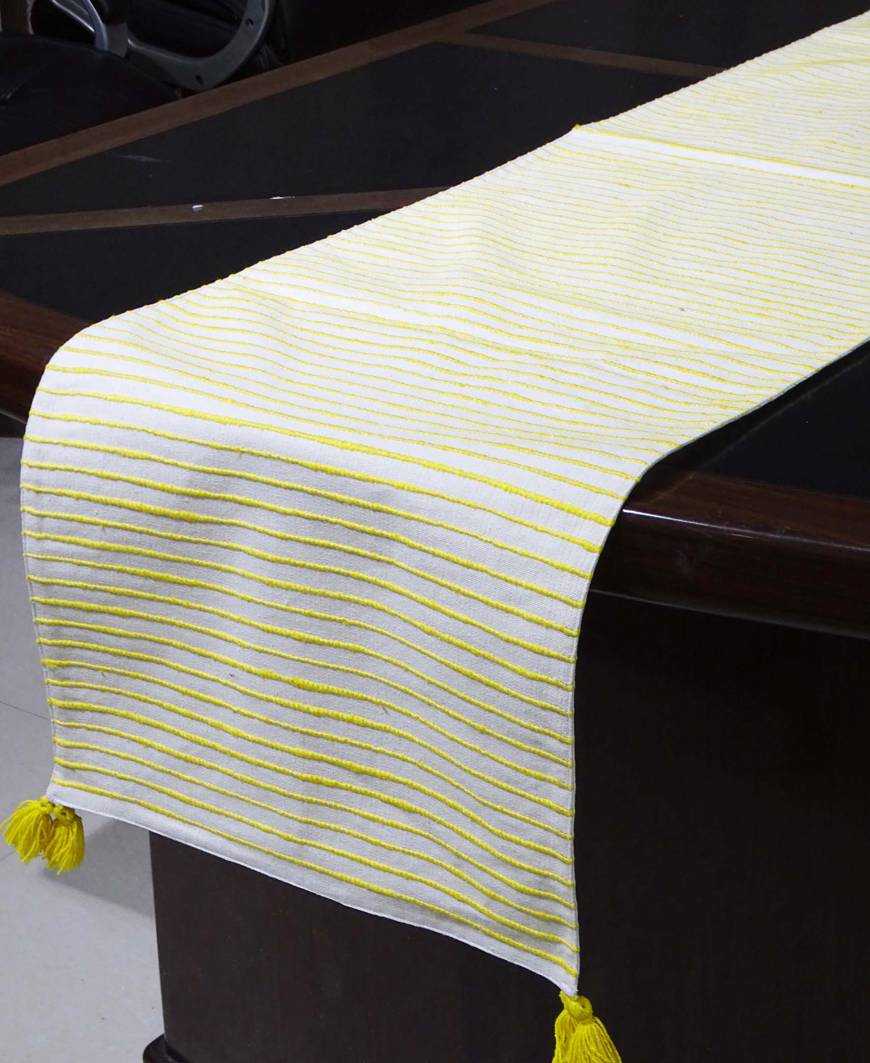 Cotton table runner with yellow and white stripes laid out on a wooden dining table