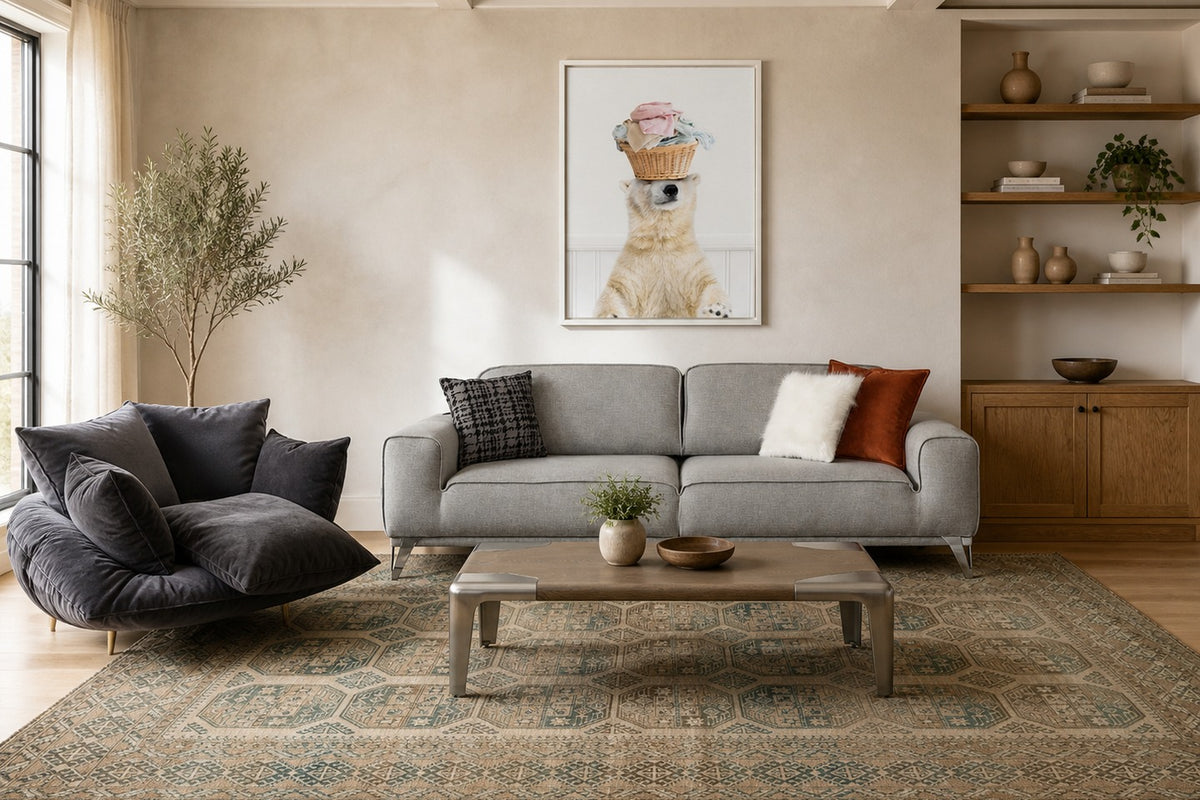 Living room with a gray sofa adorned with patterned and solid cushions, a dark cushy armchair, a wooden coffee table on a large patterned area rug, and a framed bear artwork on the wall.