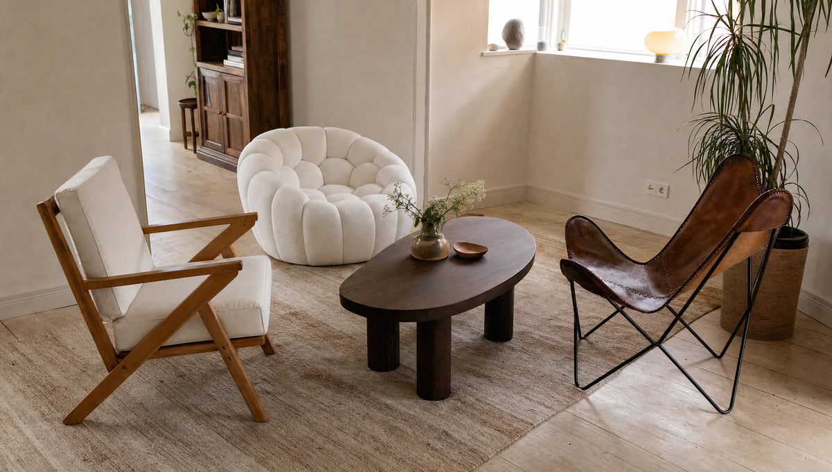 A cozy living room corner with three distinct chairs: a wooden-framed white cushioned armchair, a plush round tufted white lounge chair, and a brown leather butterfly chair with a black metal frame, arranged around a dark wooden,