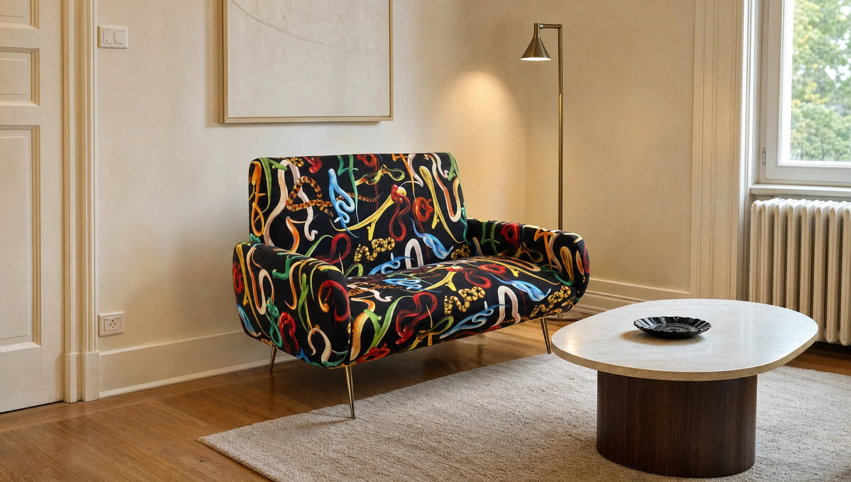 Compact black loveseat with colorful snake motifs beside a pale rug in a warm daylit room.