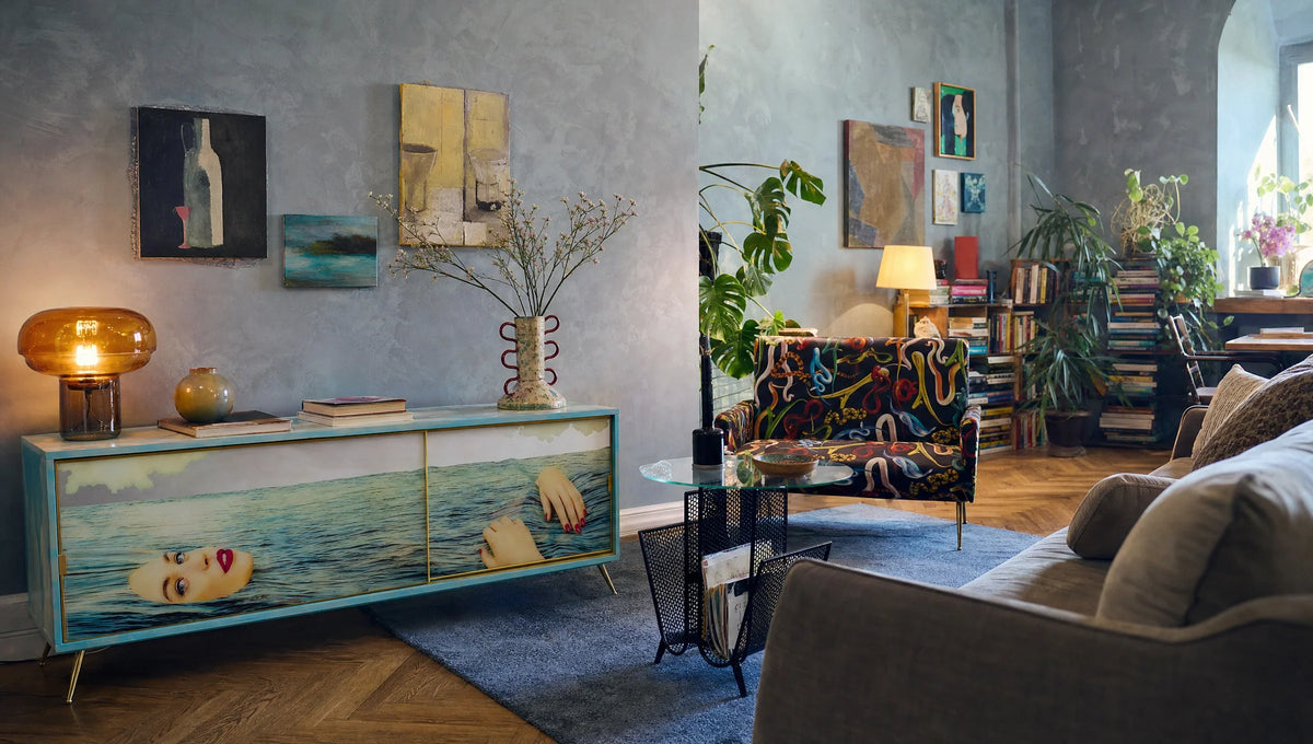 Art-filled blue-grey living room with a Sea Girl cabinet, snake-patterned loveseat and glass magazine table.