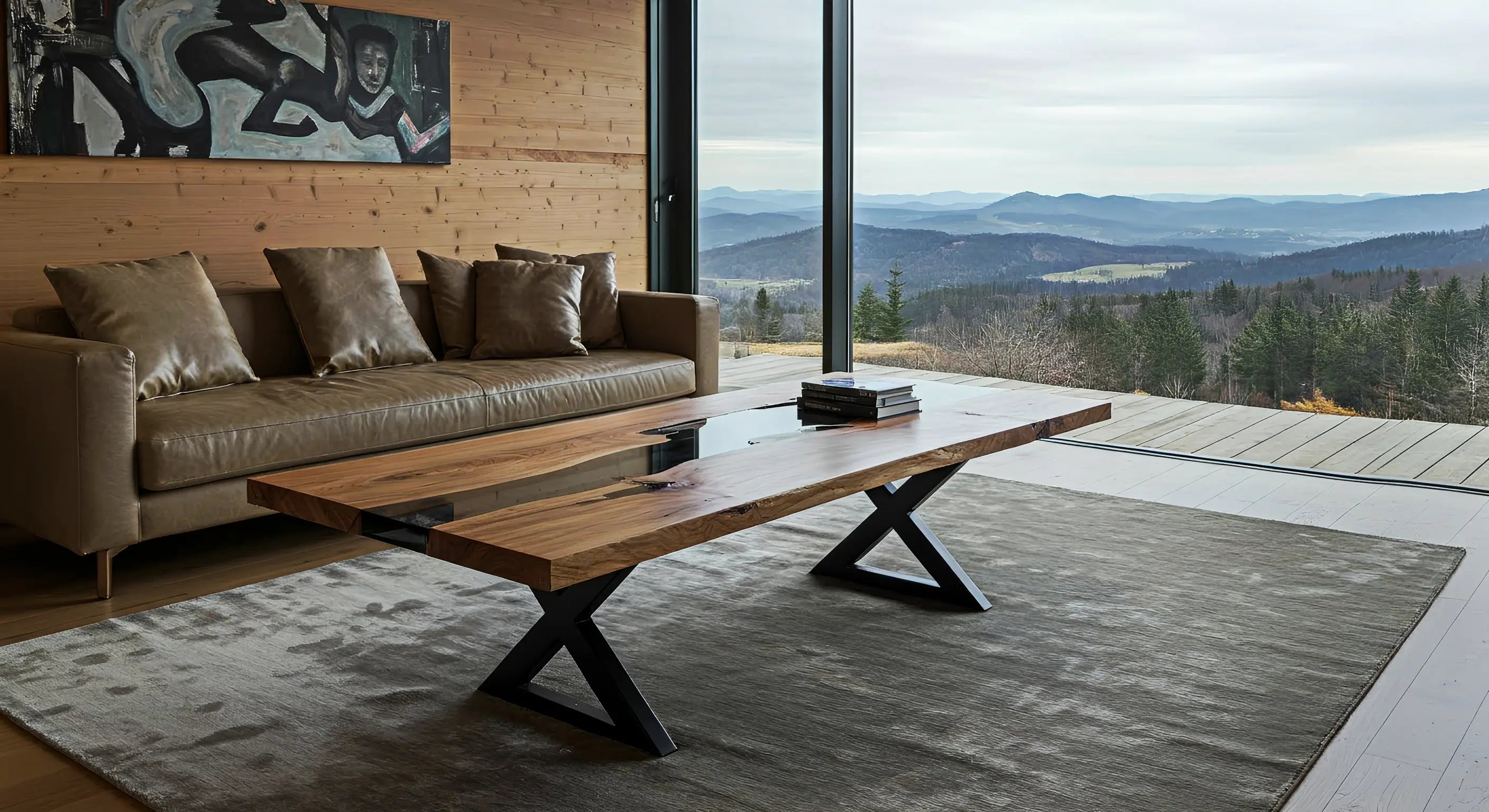epoxy coffee table in a luxury cabin living room with floor to ceiling windows and a view of the mountains.  The black resin coffee table has metal x-shaped legs resting on top of a off-white rug.  