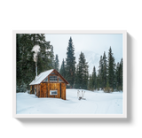 Small wooden hut with smoke rising from a chimney, surrounded by snow and evergreen trees in a winter forest landscape.