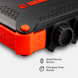 Close-up of a black and orange power bank corner with a textured top, a large black dial, and an orange button labeled with small device and charging timer icons