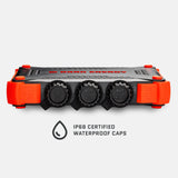 Black and bright orange rectangular power bank with three black waterproof caps labeled IN, OUT, and OUT IN/OUT, shown from the side on a white background.