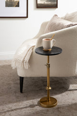 Small adjustable table with a round black marble top and brass metal base next to a cream boucle upholstered sofa with a beige throw and pillow.