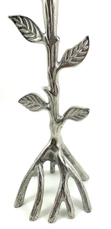 Silver metal candle holder shaped like a tree branch with detailed textured leaves and roots forming the base on a white background.