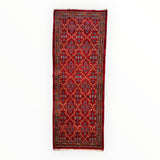 Narrow rectangular vintage Mashhad wool runner with dense red background and intricate geometric floral motifs in blue, white, and black, framed by detailed red and black borders.