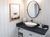 Rectangular wall art featuring three small pigs in a vintage white clawfoot bathtub, framed in light wood, hung above a black countertop with an oval mirror.