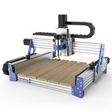 Desktop CNC router with aluminum frame and blue corner brackets, featuring a spindle mounted on a vertical gantry above a slotted wooden work surface.