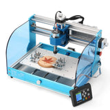Compact desktop blue and silver CNC router with transparent blue safety guard, engraving a maple leaf onto a circular wood piece secured on the workbed, with a black control panel attached