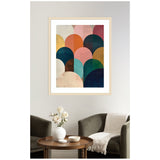 Framed minimalist abstract art with overlapping semi-circles in jewel tones of navy, coral, ochre, and pink, hanging above a cozy sitting area with dark armchairs and a wooden table.