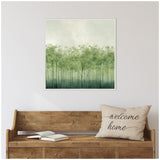 Square framed canvas print depicting abstract green tree shapes with thin trunks and leafy canopies against a light background, hanging above a rustic wooden bench with a 'welcome home' pillow and open books.