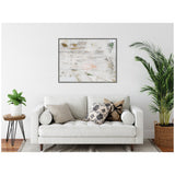 Framed abstract canvas wall art with muted white, beige, and green brushstrokes hanging above a white sofa accented by patterned pillows and flanked by leafy plants.