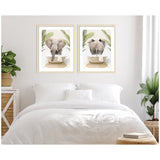 Two framed prints above a white bed showing an elephant in a bathtub, with one print of the elephant facing front and the other from behind, surrounded by green palm leaves.