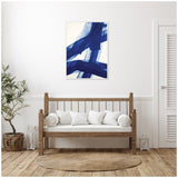 Abstract wall art with broad cobalt blue brushstrokes on white canvas above a wooden bench with white pillows in a minimalist living space.