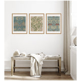 Three framed Sylvie William Morris posters with intricate floral and leaf patterns in muted blue, green, and beige tones, displayed above a wooden bench with light fabric draped over it.