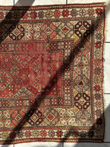 Antique Turkish wool prayer rug with intricate geometric and floral patterns in red, beige, and brown tones, featuring a central diamond motif and bordered edges.