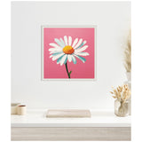 Square white-framed canvas featuring a single white daisy with a yellow center on a solid pink background, hung above a light wood desk with neutral decor.