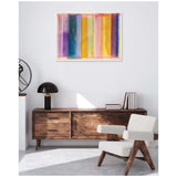 Abstract framed canvas with vertical translucent stripes in purple, blue, yellow, and orange hanging above a wooden sideboard and white cushioned chair with wooden frame.