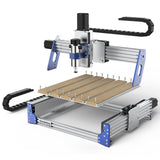 Compact desktop CNC router with aluminum frame and blue corner brackets, equipped with spindle motor and wooden work surface secured by clamps.