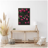 Framed canvas of dark pink tulip buds against deep green foliage, hung above a rustic wooden console table in a bright, minimalist room.